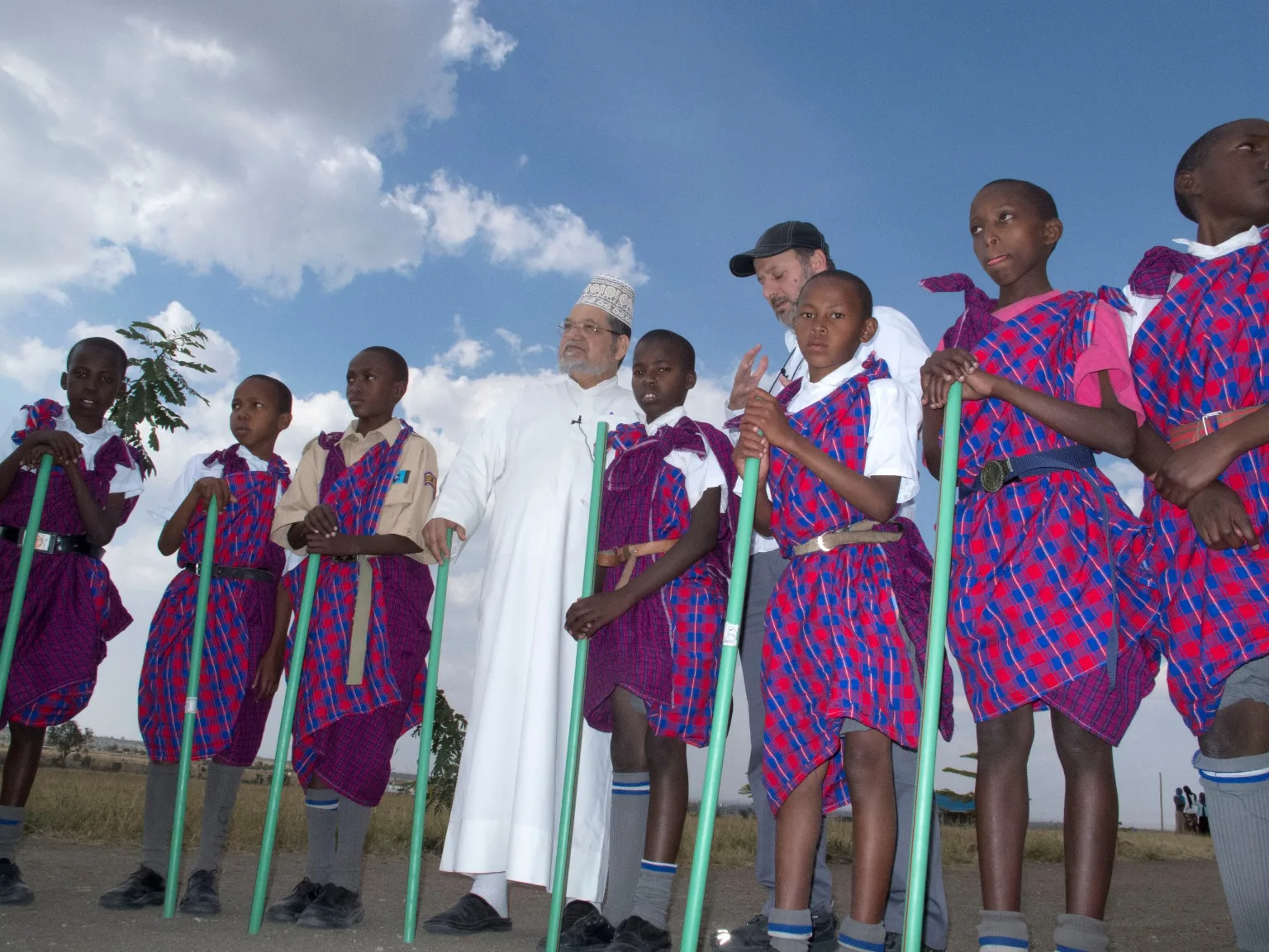 Dr. Al-Sumait standing among Maasai students in red shuka under a wide sky