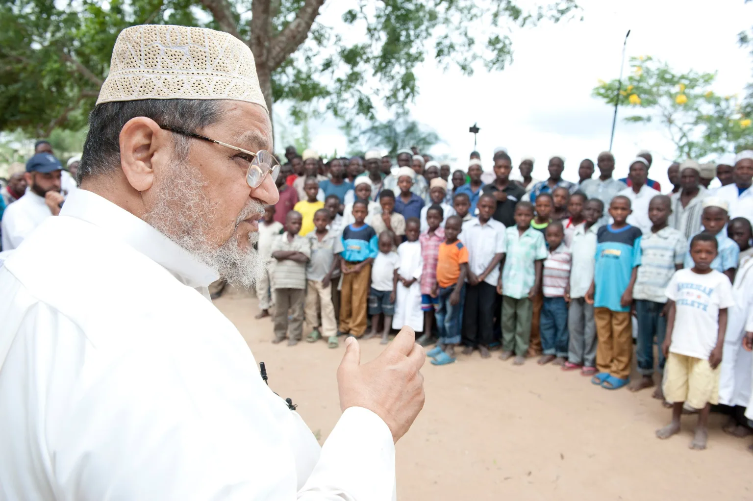 Dr. Al-Sumait speaking to a crowd of children gathered under a tree
